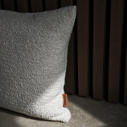 Textured beige pillow with a brand tag on a dark background