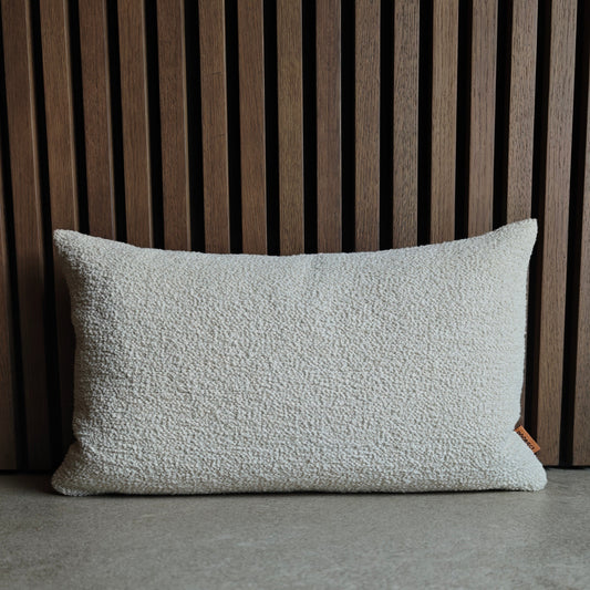 Textured off white boucle pillow on concrete surface with a wooden panel background