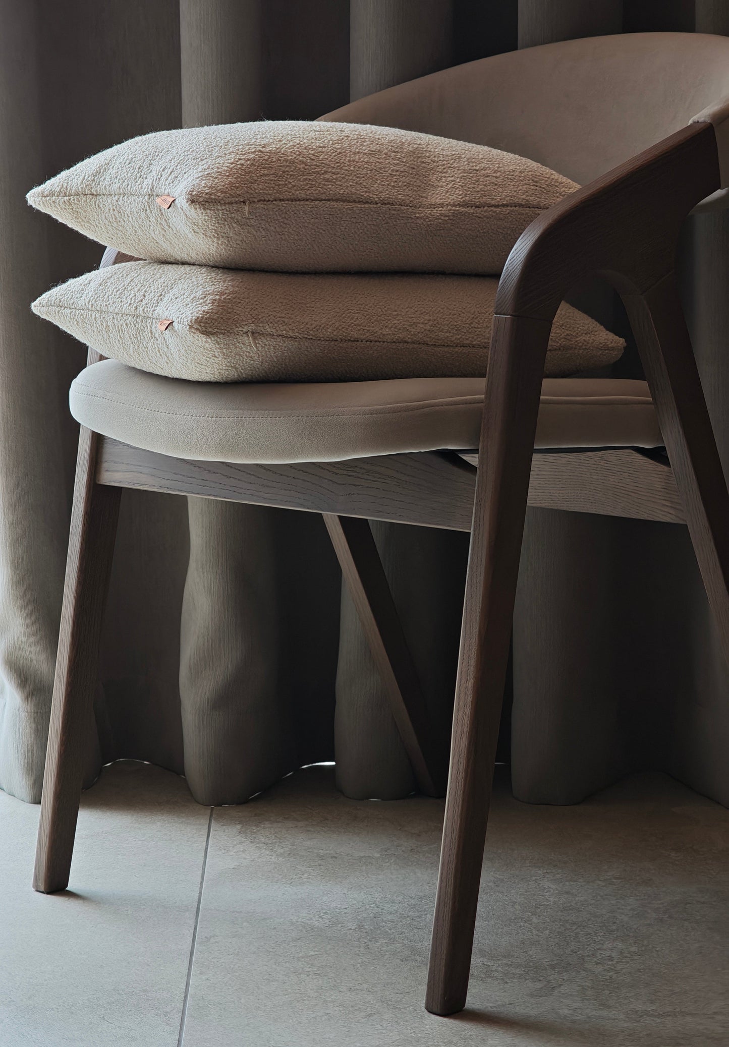 Two beige Boucle cushions stacked on the chair agains night curtains