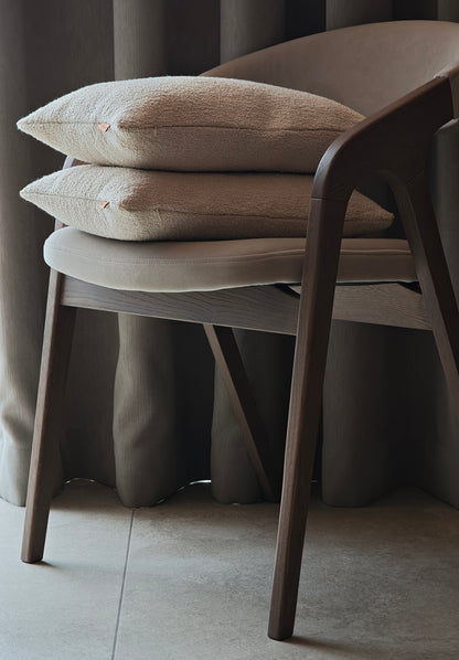 Two beige Boucle cushions stacked on the chair agains night curtains
