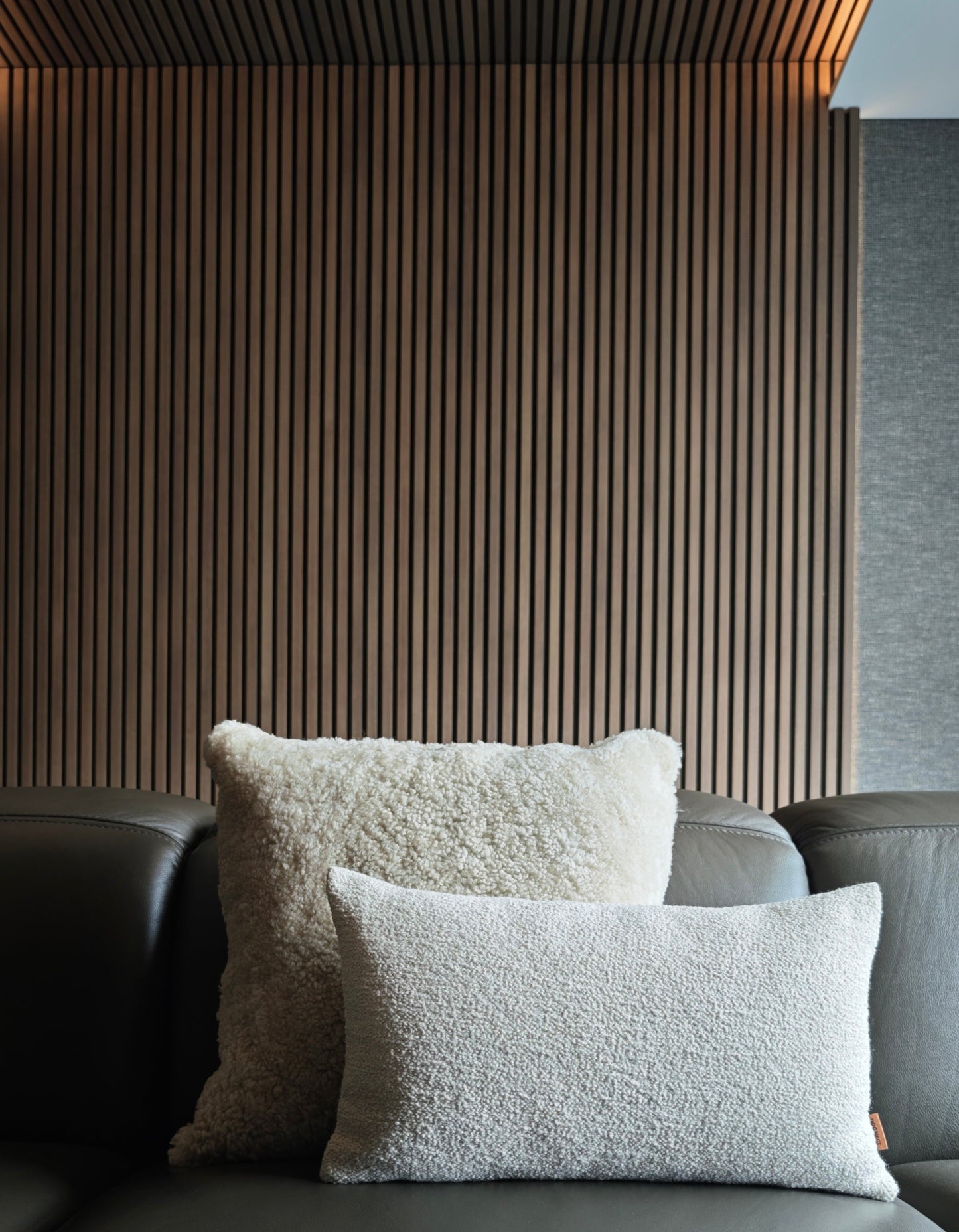 Beige Sheepskin and Off white boucle cushion set on dark leather sofa with wooden slats background