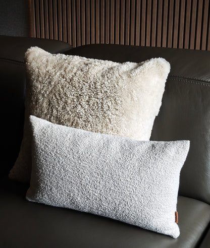 Two textured pillows on a dark leather sofa with a wooden beam wall
