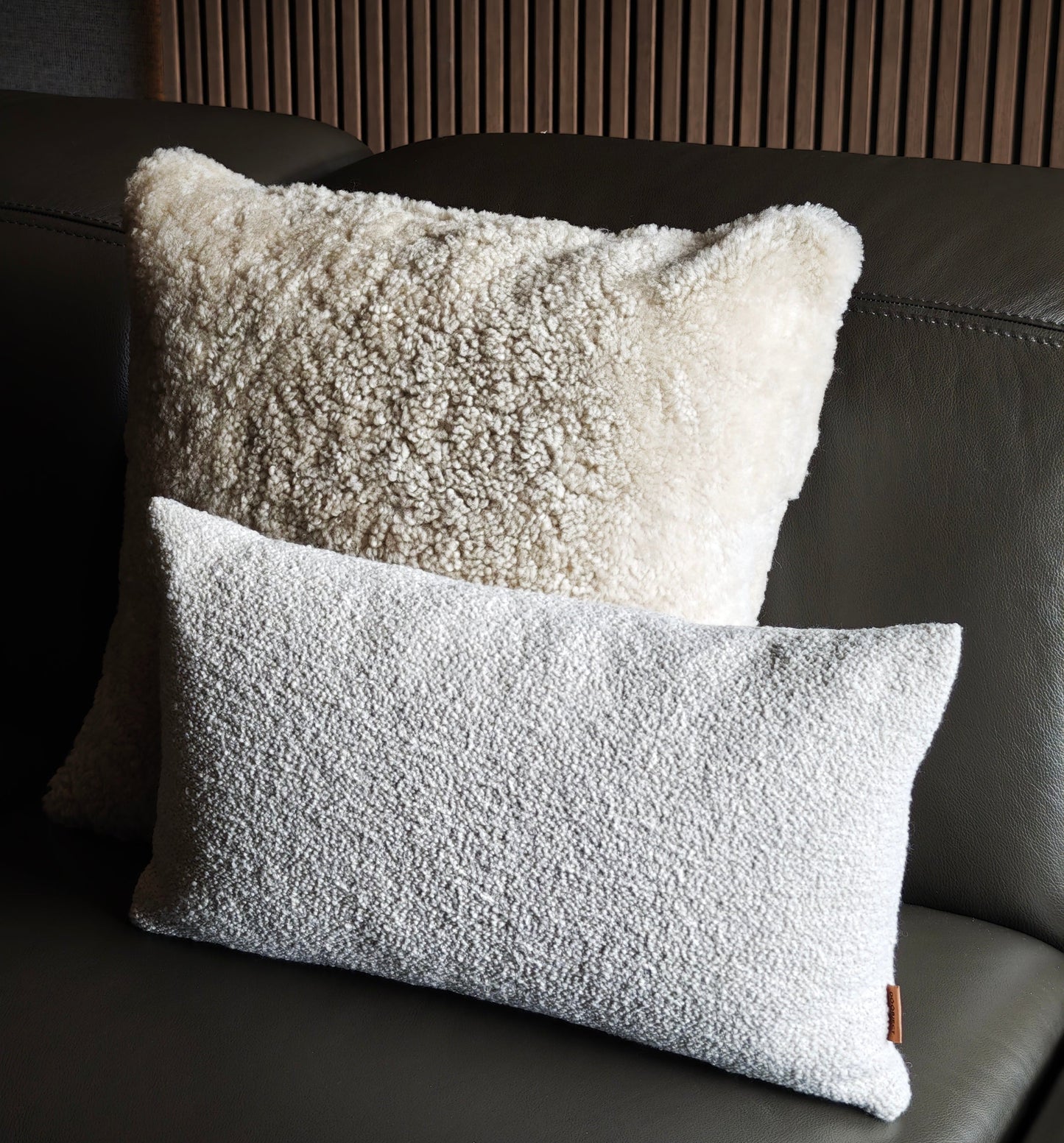 Two textured pillows on a dark leather sofa with a wooden headboard.