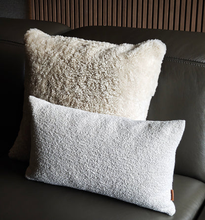 Two textured pillows on a dark leather sofa with a wooden headboard.