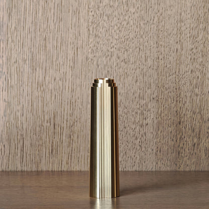 Brass cylindrical candle holder on a wooden surface with a neutral background