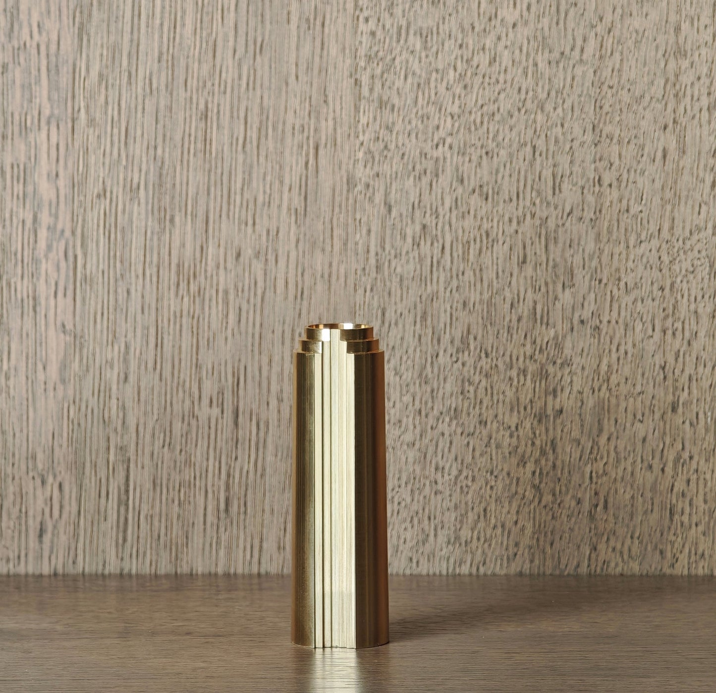 Brass cylindrical object on a wooden surface with a neutral background