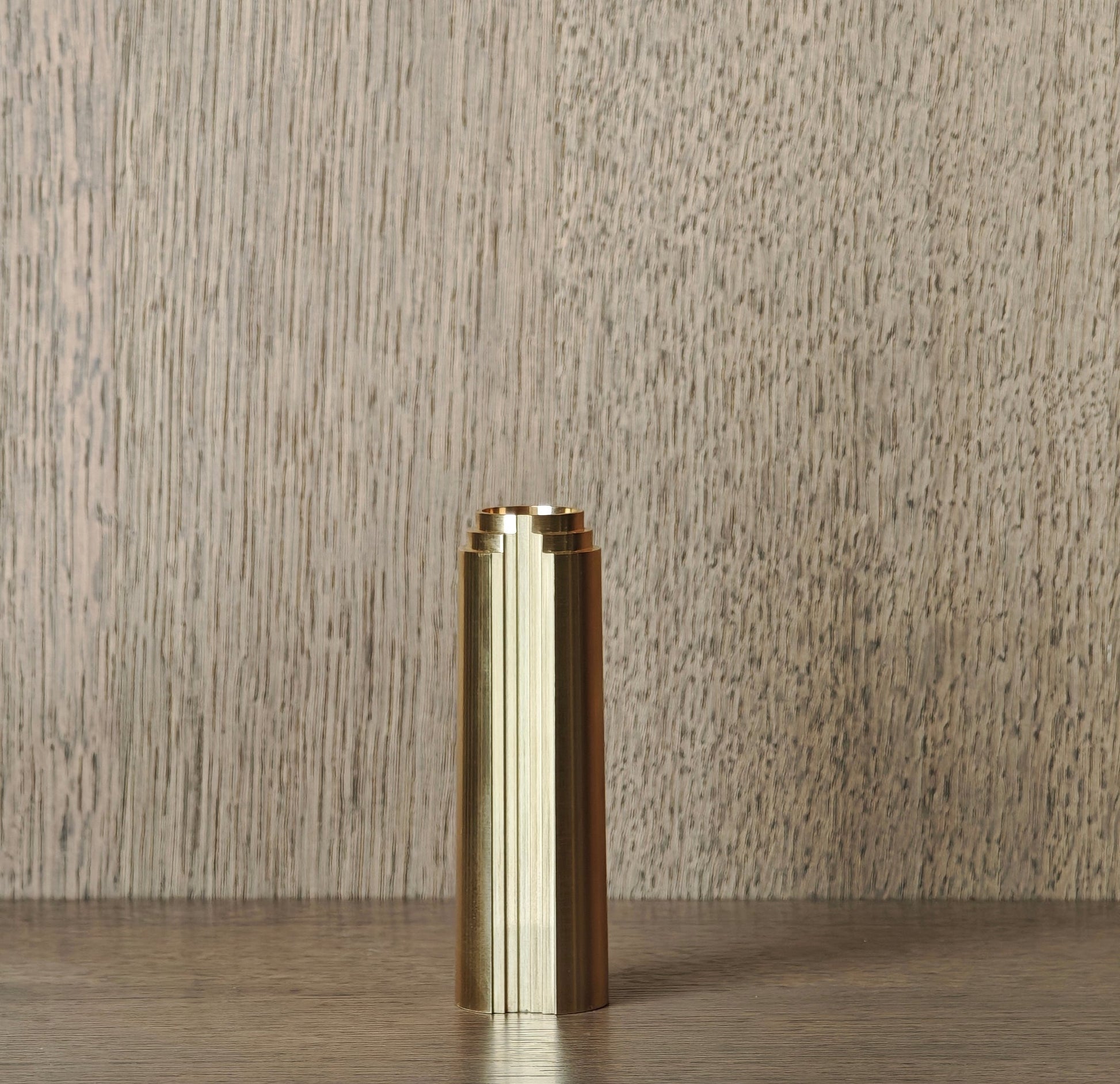 Brass cylindrical object on a wooden surface with a neutral background