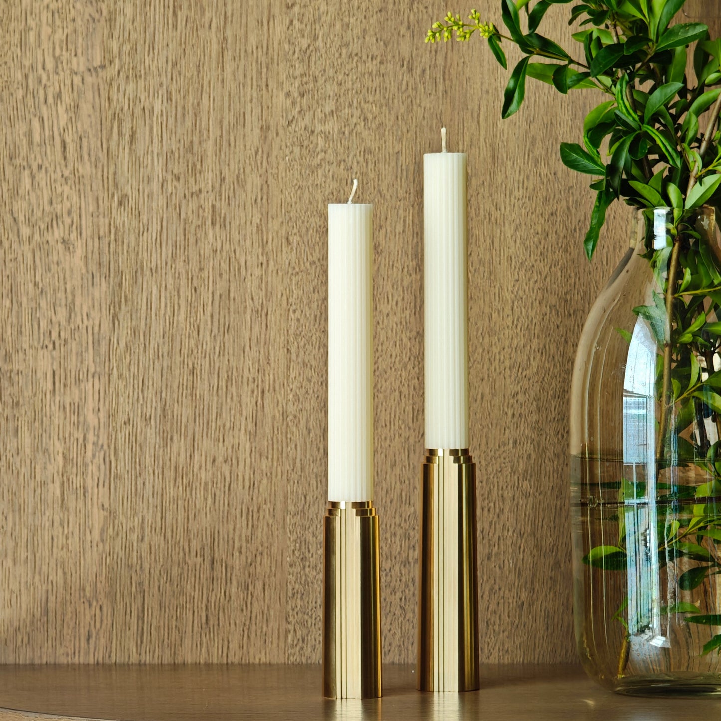 Wooden cabinet with two white candles and a vase with greenery on a neutral background