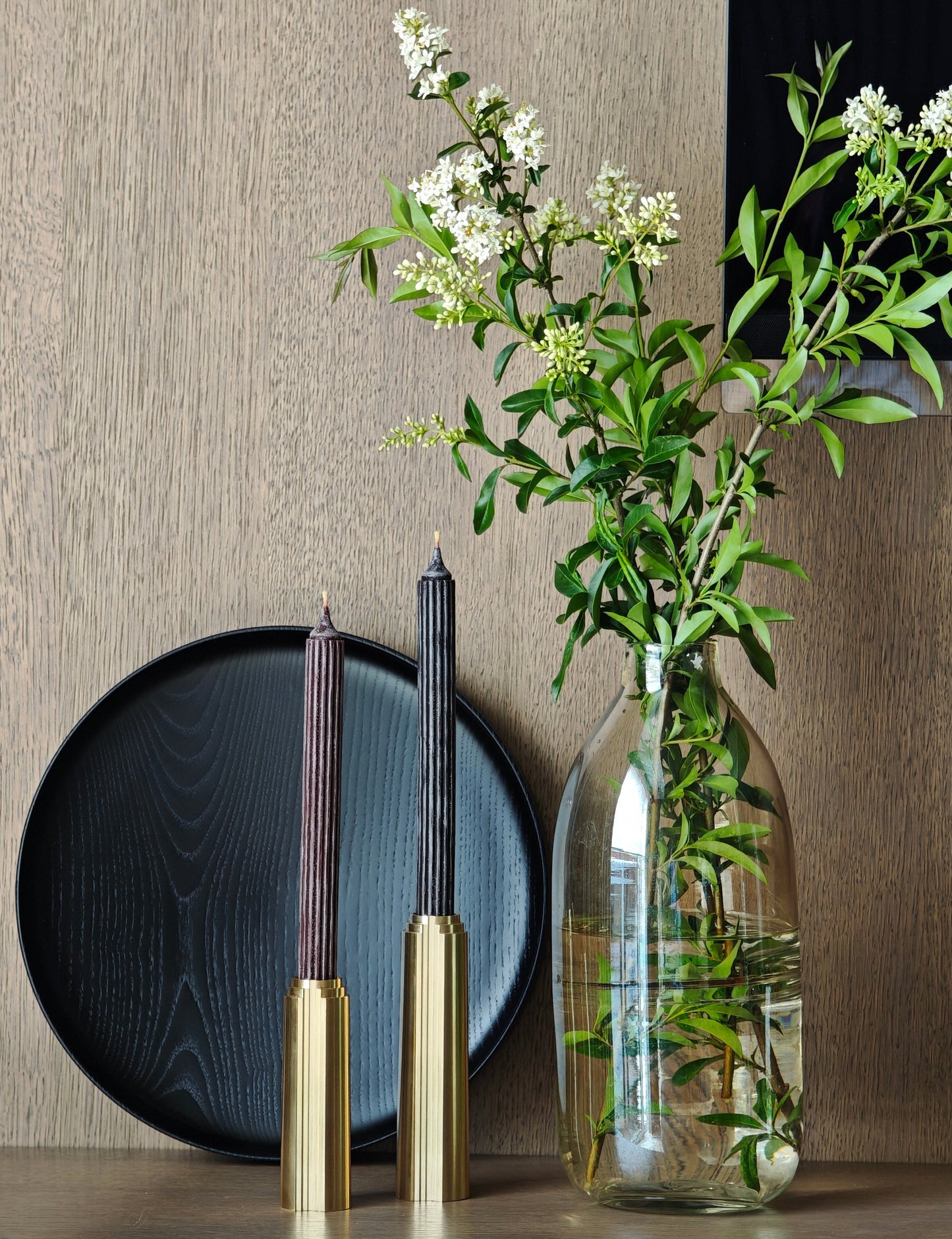 Decorative setting with a vase of flowers, candles, and a plate on a wooden surface.