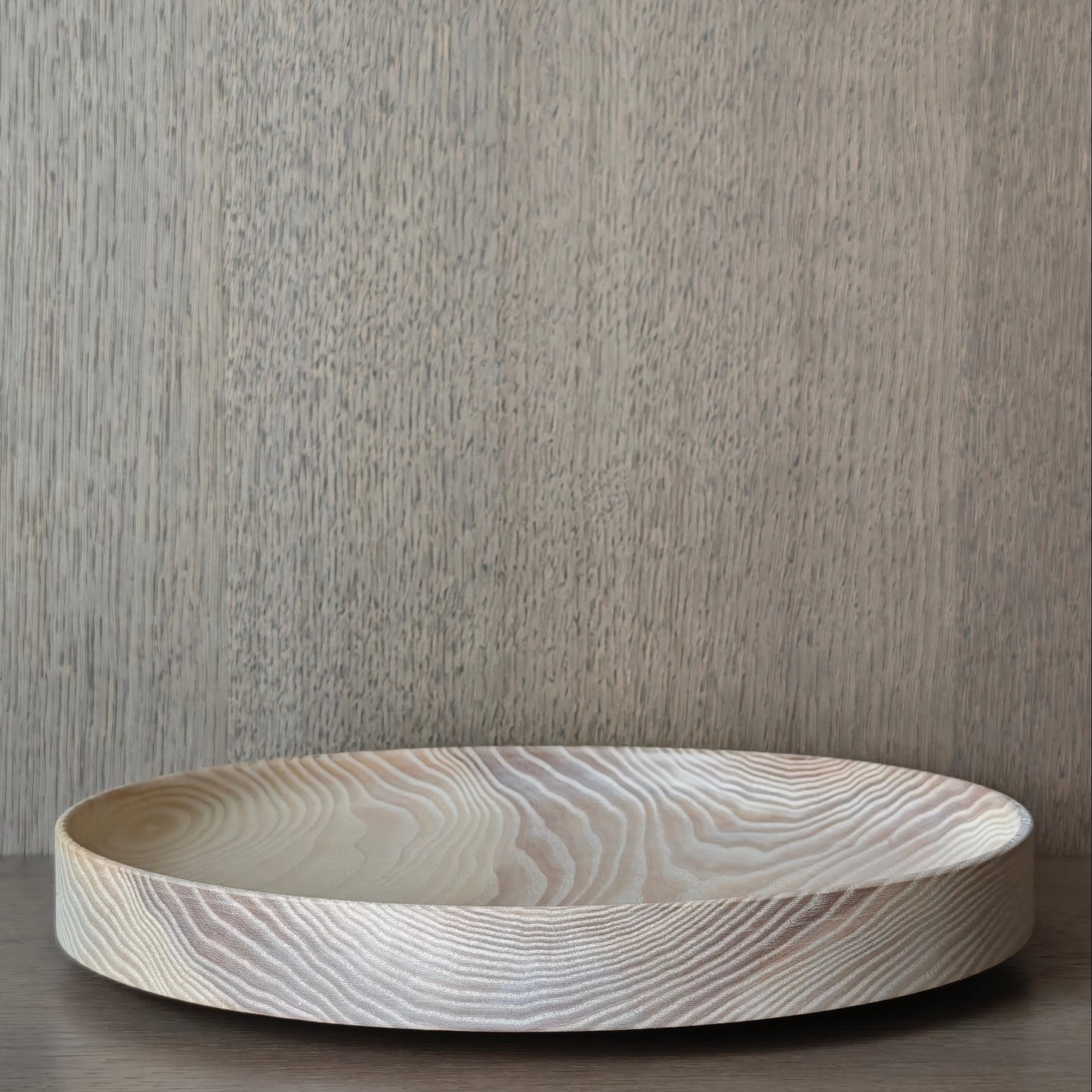 Round wooden dish with exposed pattern on a wooden surface and neutral background