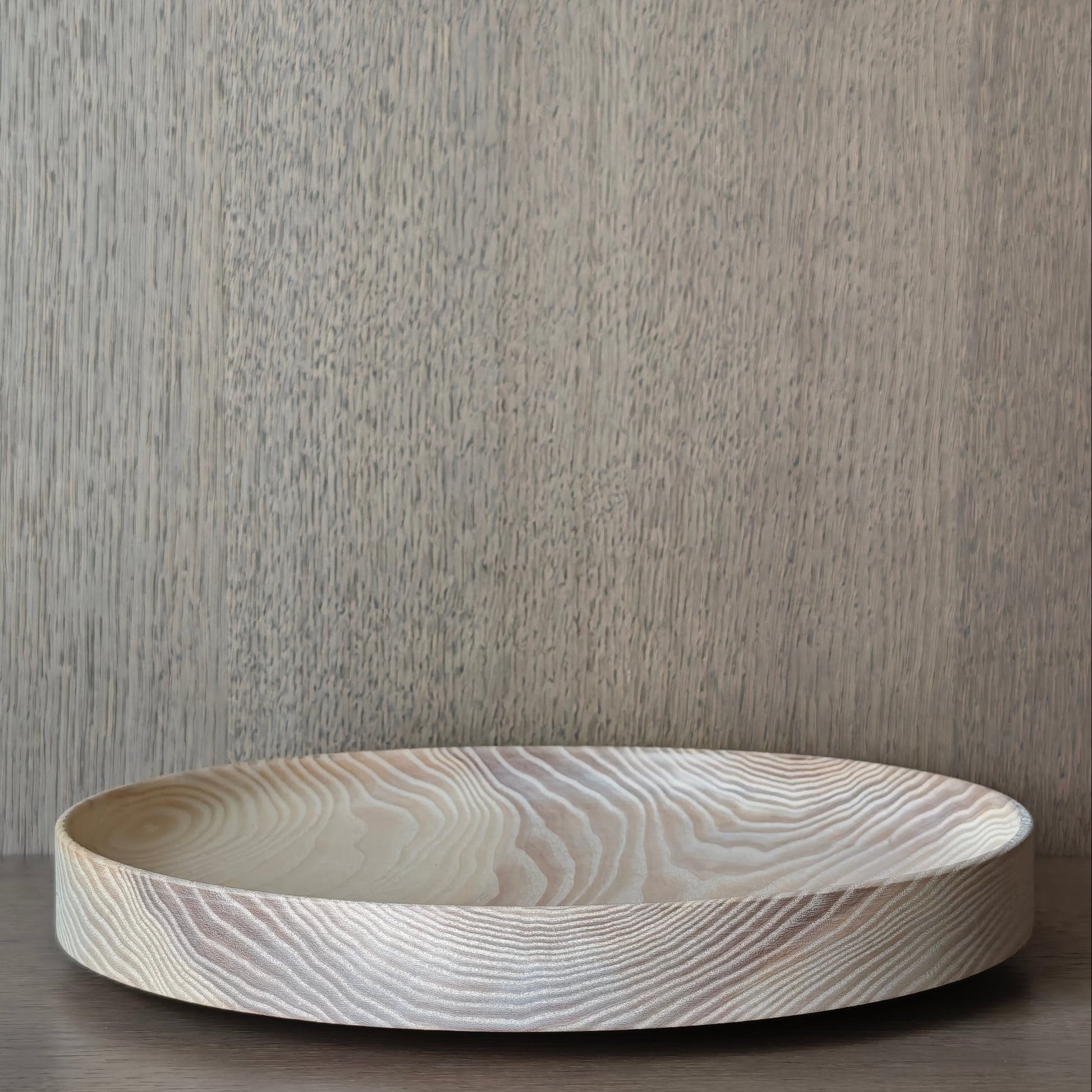 Round wooden dish with exposed pattern on a wooden surface and neutral background