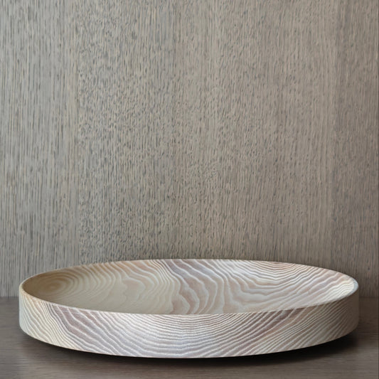 Round wooden dish with exposed pattern on a wooden surface and neutral background
