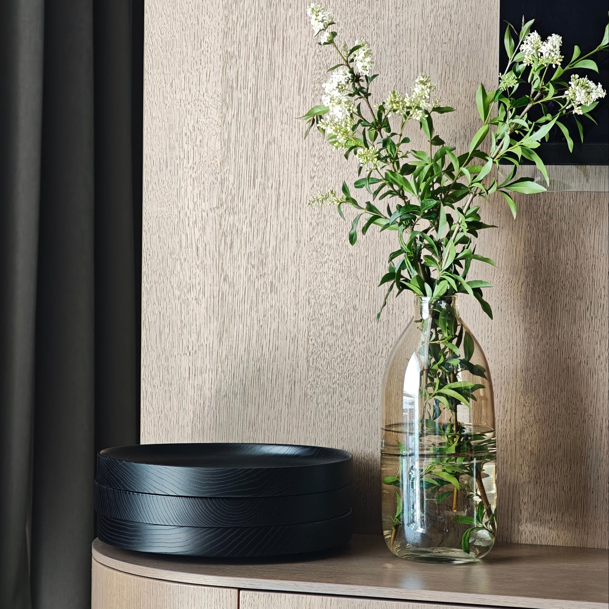 Decorative setup with a black bowl and glass vase with flowers on a wooden surface.