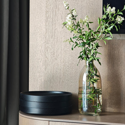 Decorative setup with a black bowl and glass vase with flowers on a wooden surface.