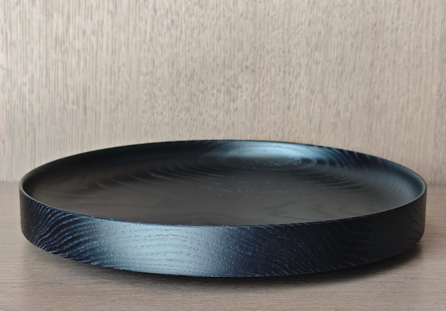 Black round wooden tray on a wooden surface with a neutral background