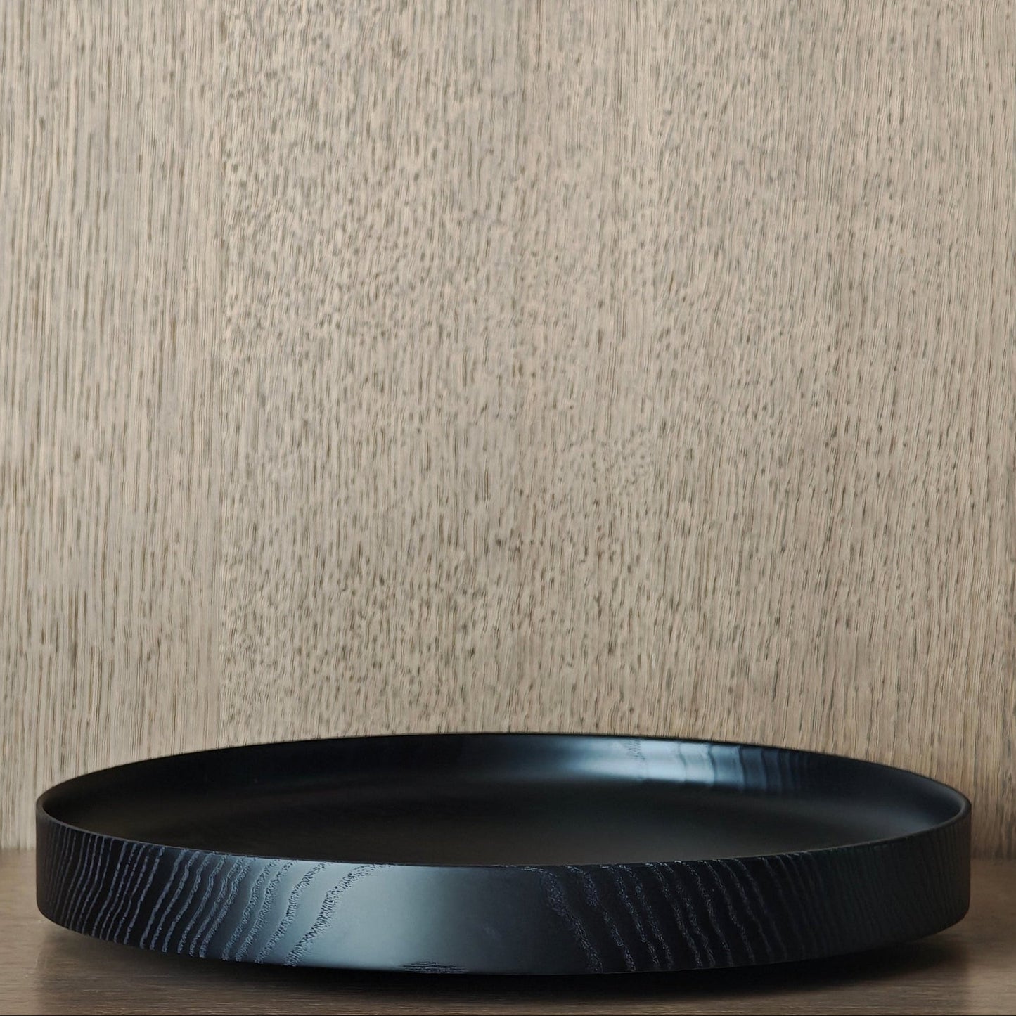 Round black wooden dish with grain exposed against wooden panelling