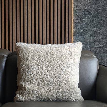 Textured white pillow on a dark grey sofa against a striped wooden slats wall and textured dark Romo wallpaper.