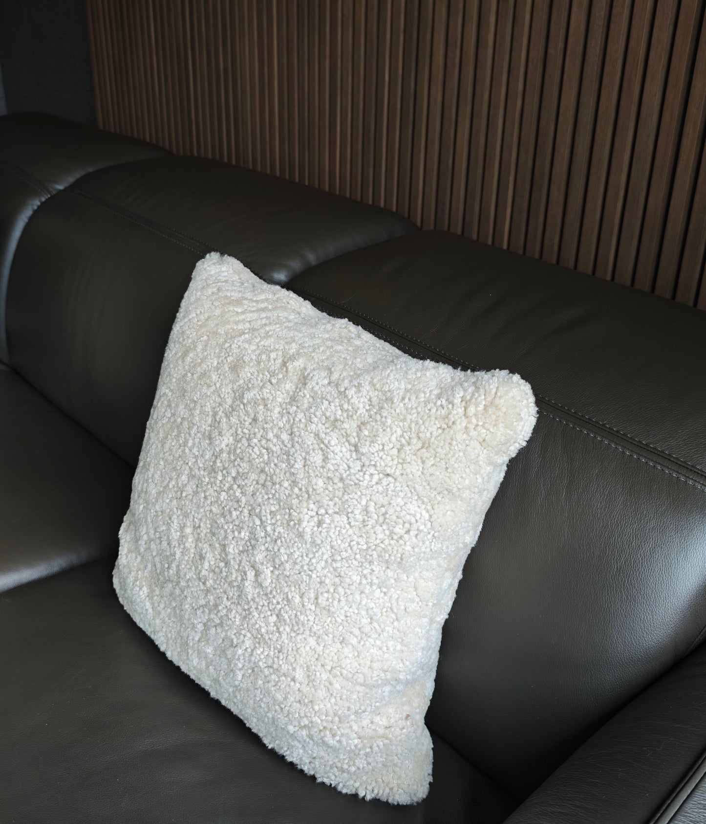 White textured pillow on a dark brown leather sofa against a wooden slats paneled wall.