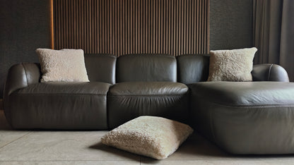 Textured off white sheepskin cushion on dark leather sofa against wooden slats paneling with wallpaper and curtains and tiles flooring