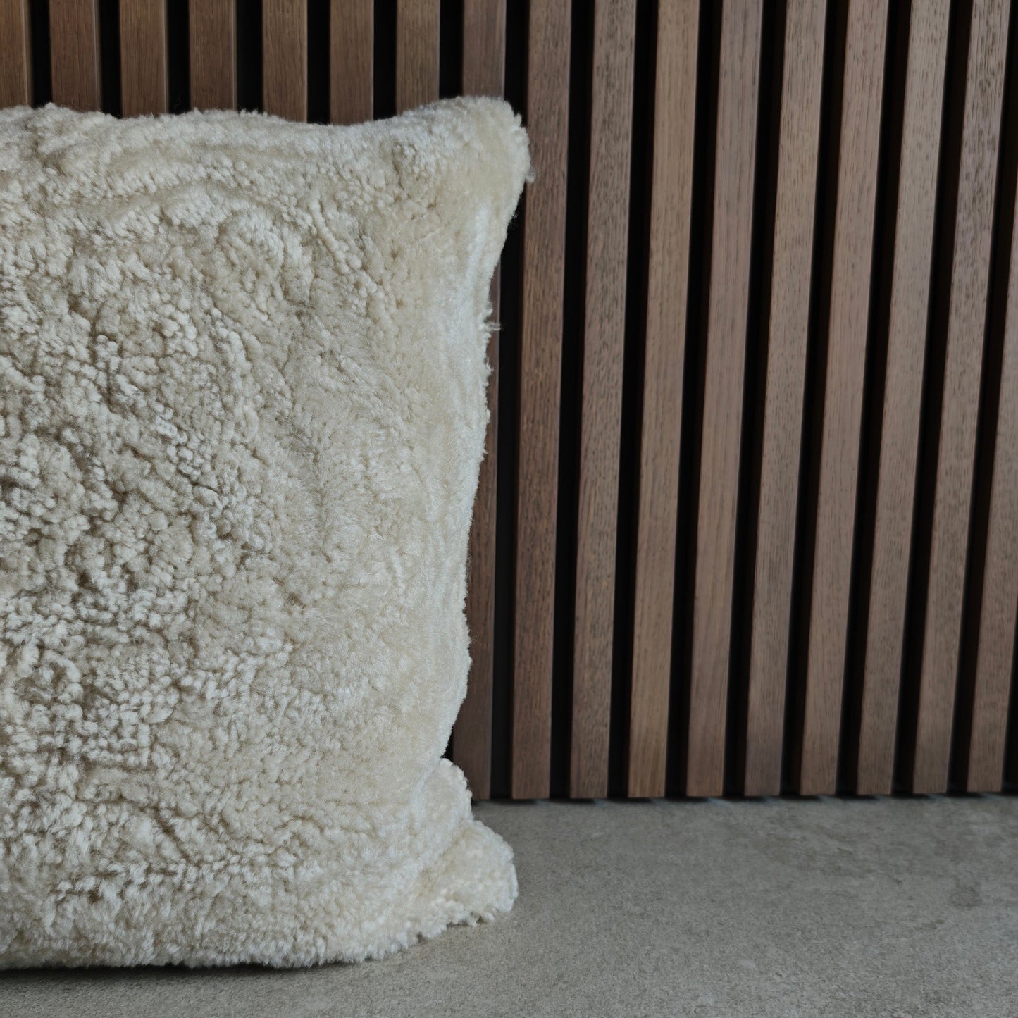 Textured off white sheepskin pillow on a grey tile surface with a wooden slat background