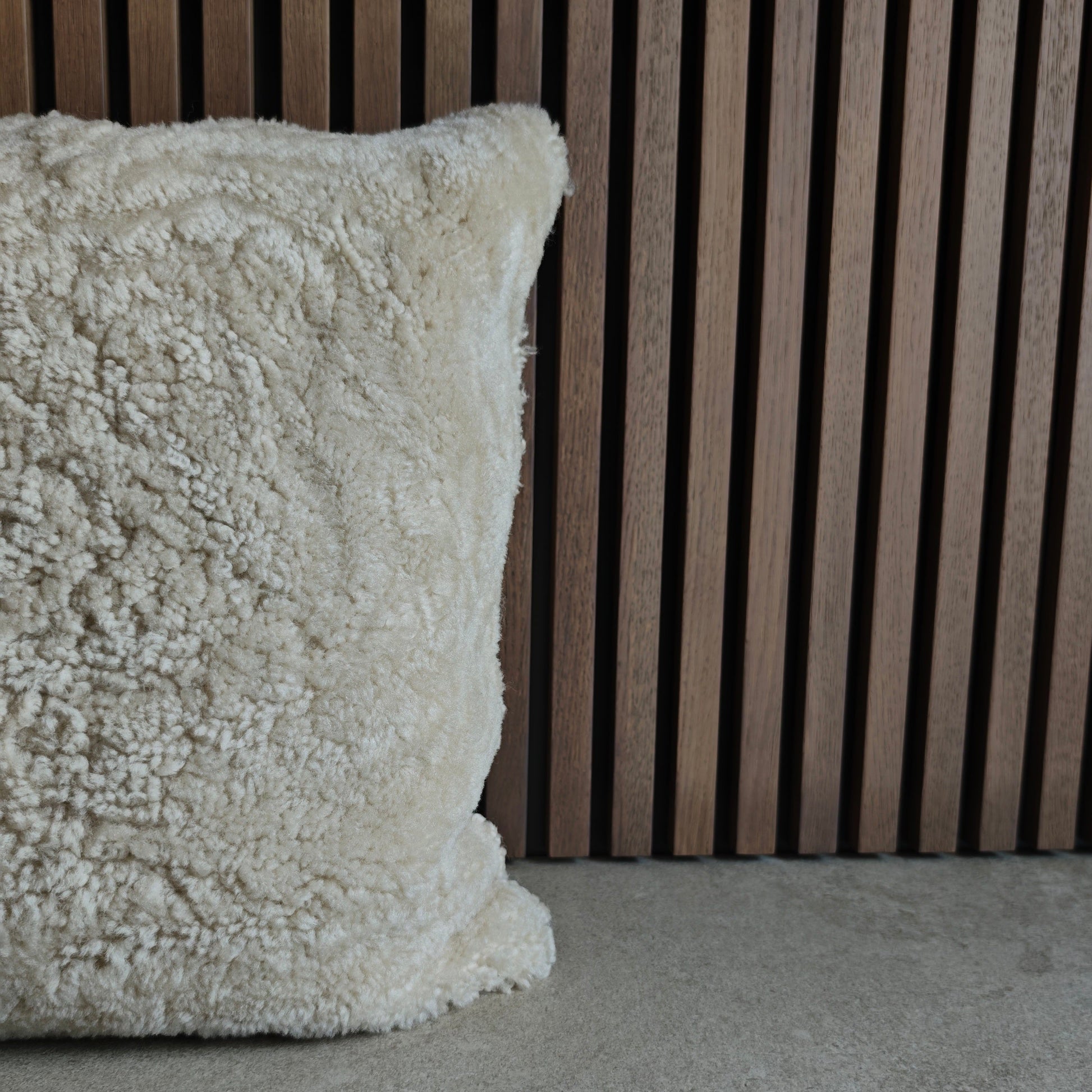 Textured off white sheepskin pillow on a grey tile surface with a wooden slat background