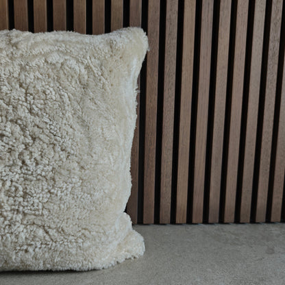 Textured off white sheepskin pillow on a grey tile surface with a wooden slat background