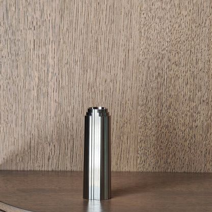 Stainless steel candle holder on a wooden surface with a wooden wall panel