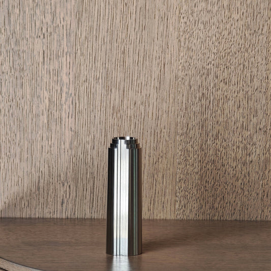 Stainless steel candle holder on a wooden surface with a wooden wall panel