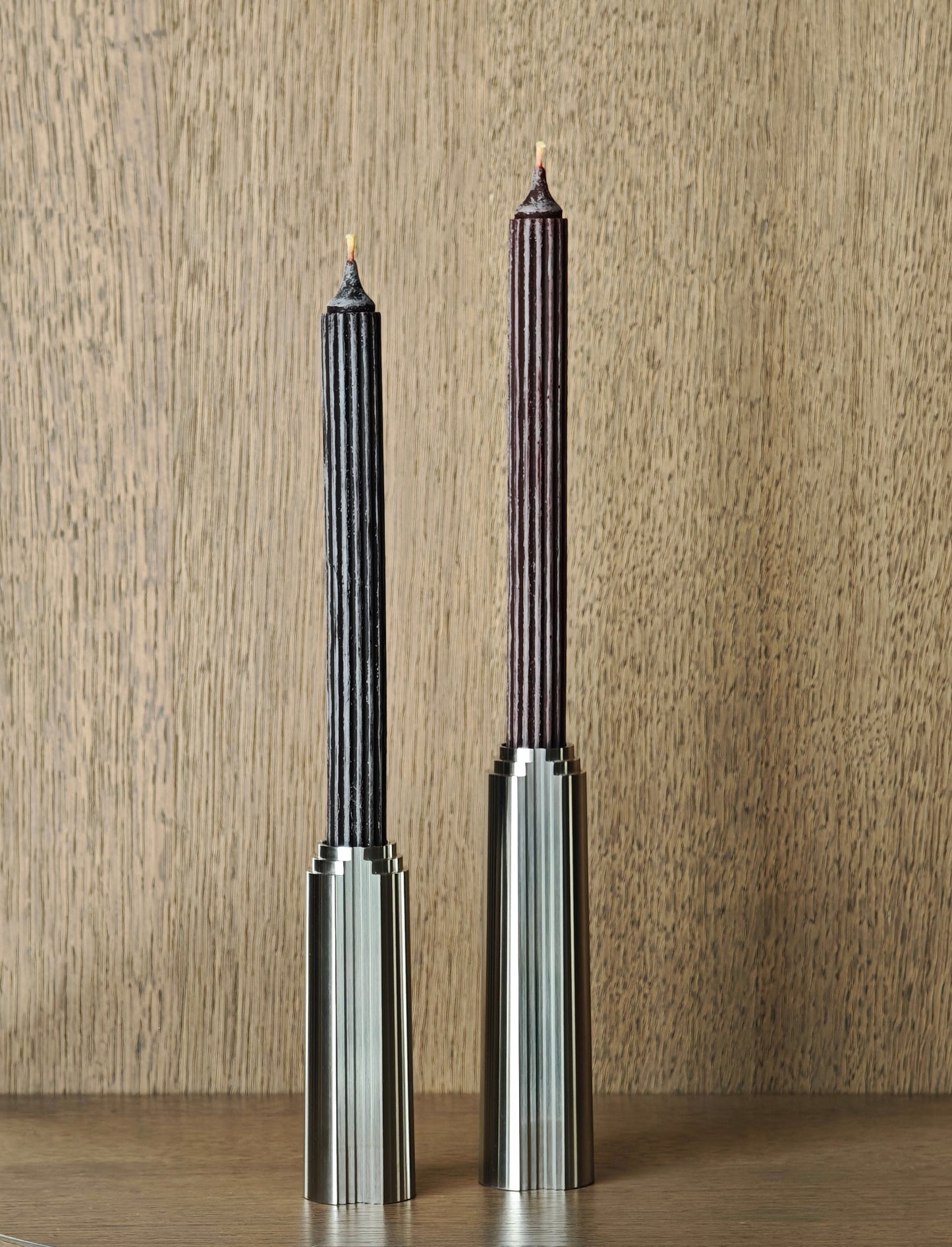 A pair of stainless steel candle holders with textured beewax candles on wooden surface