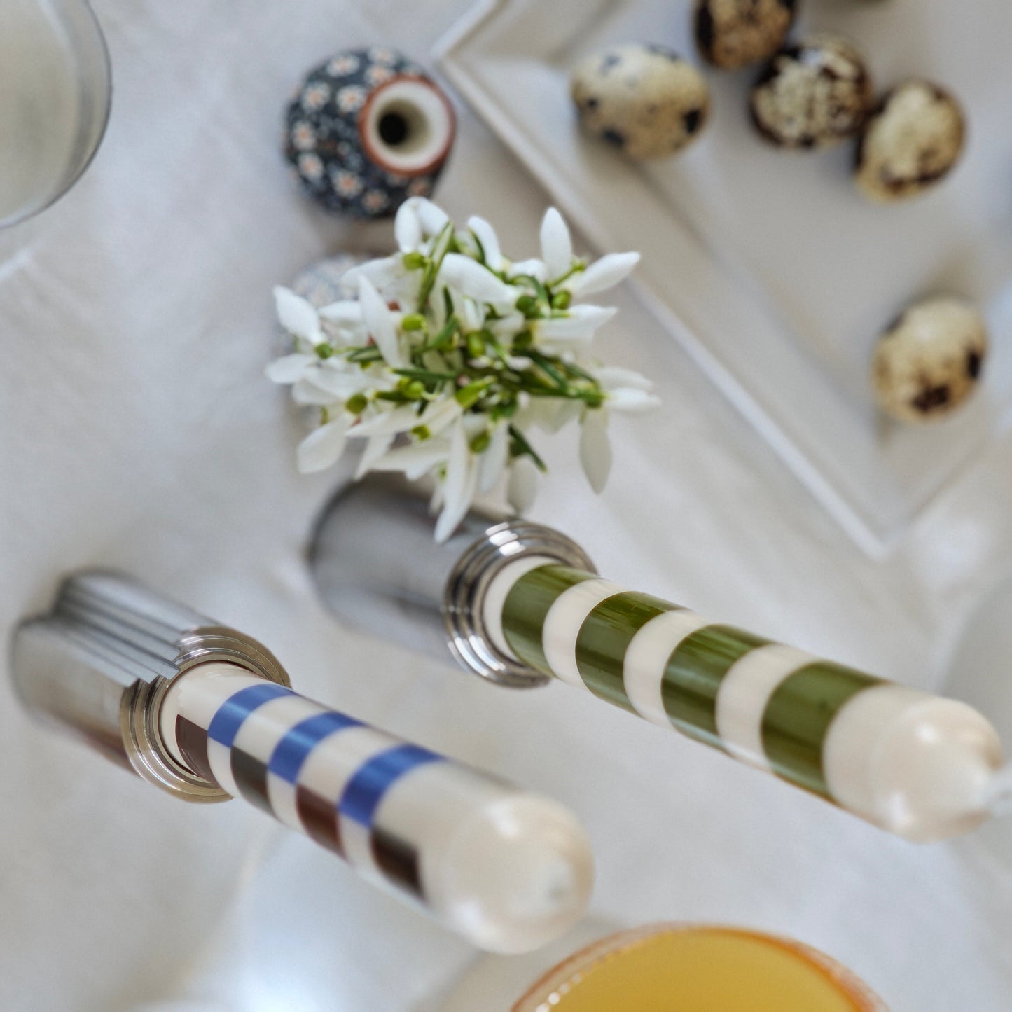Top-down view of a table setting with candle holders, glasses, a flower arrangement, and white tablecloth.