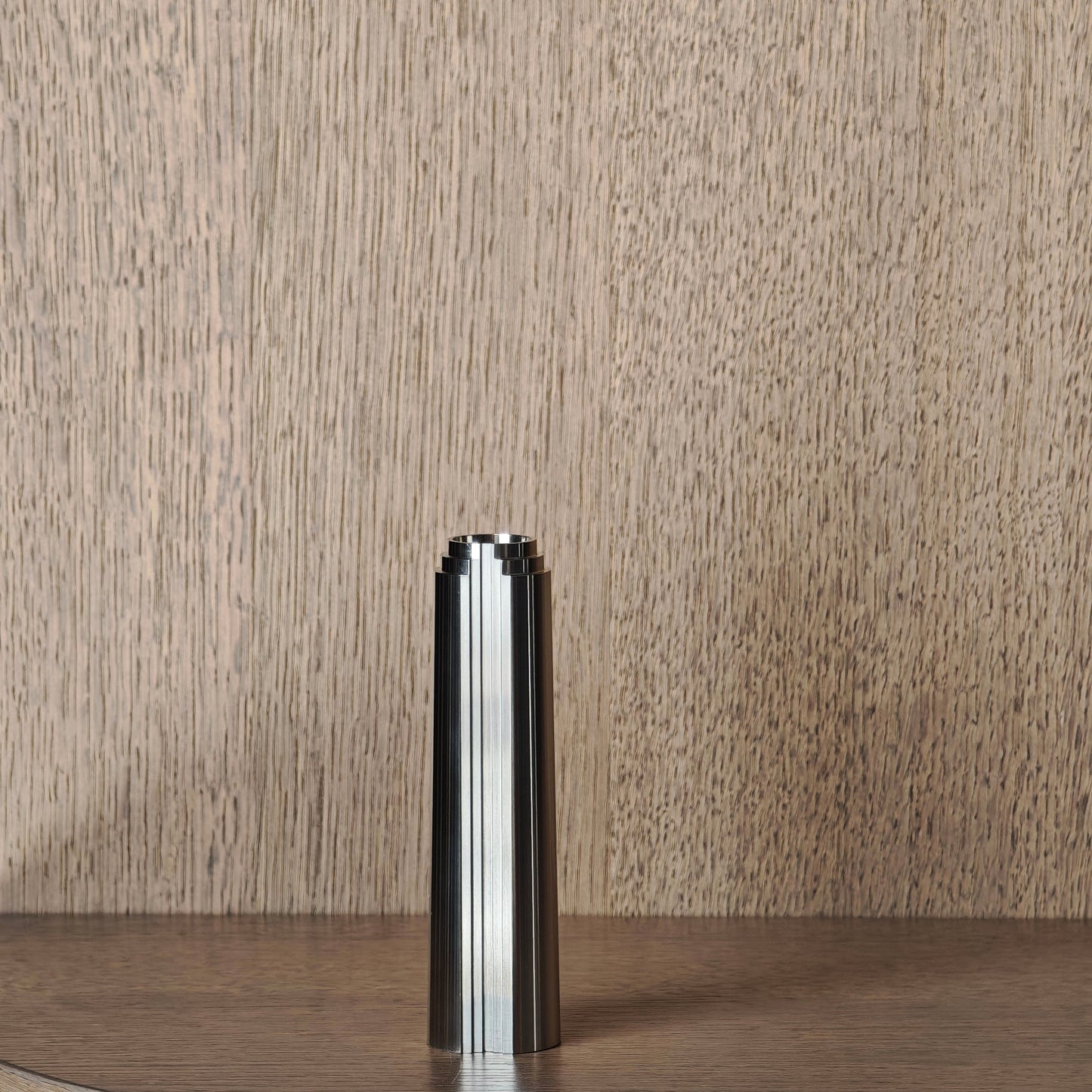 Stainless steel cylindrical candle holder on a wooden surface with a neutral background