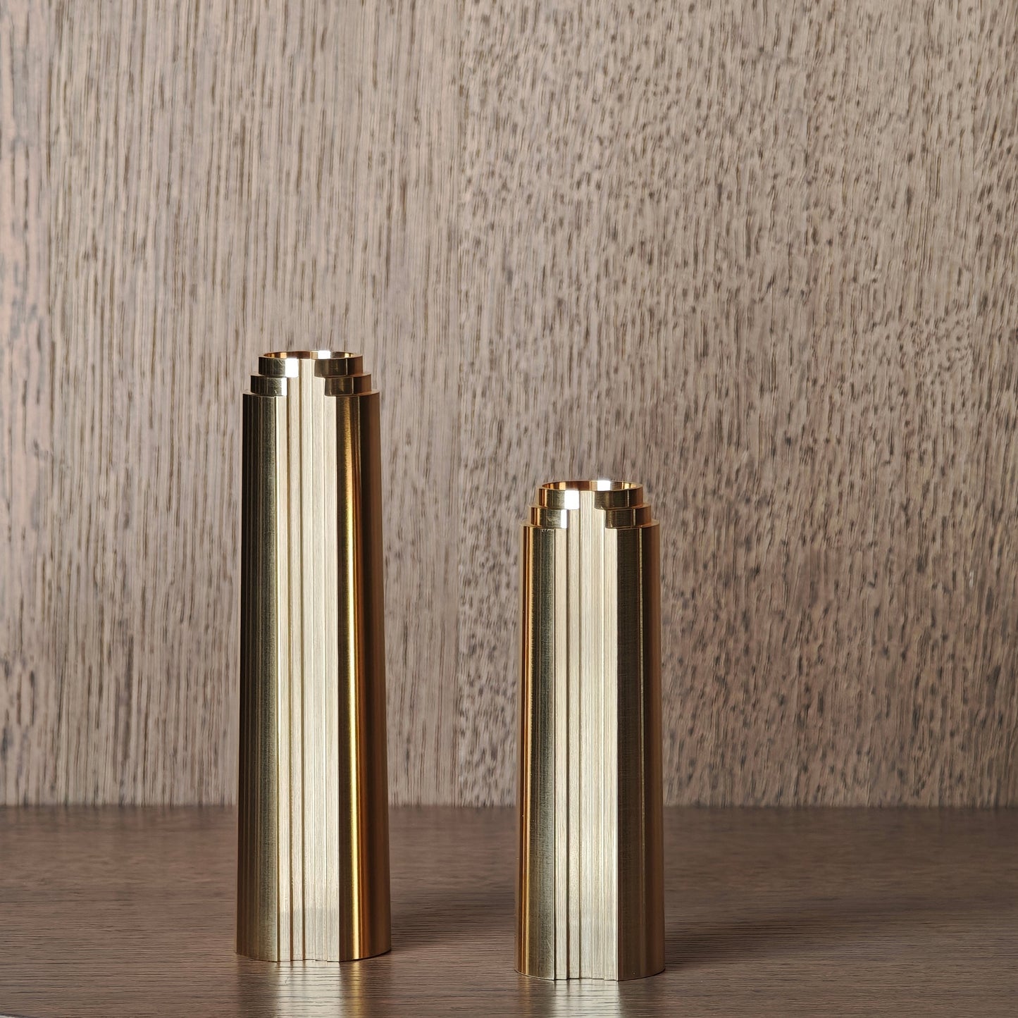 Two brass cylindrical candle holders on a wooden surface with a wooden background
