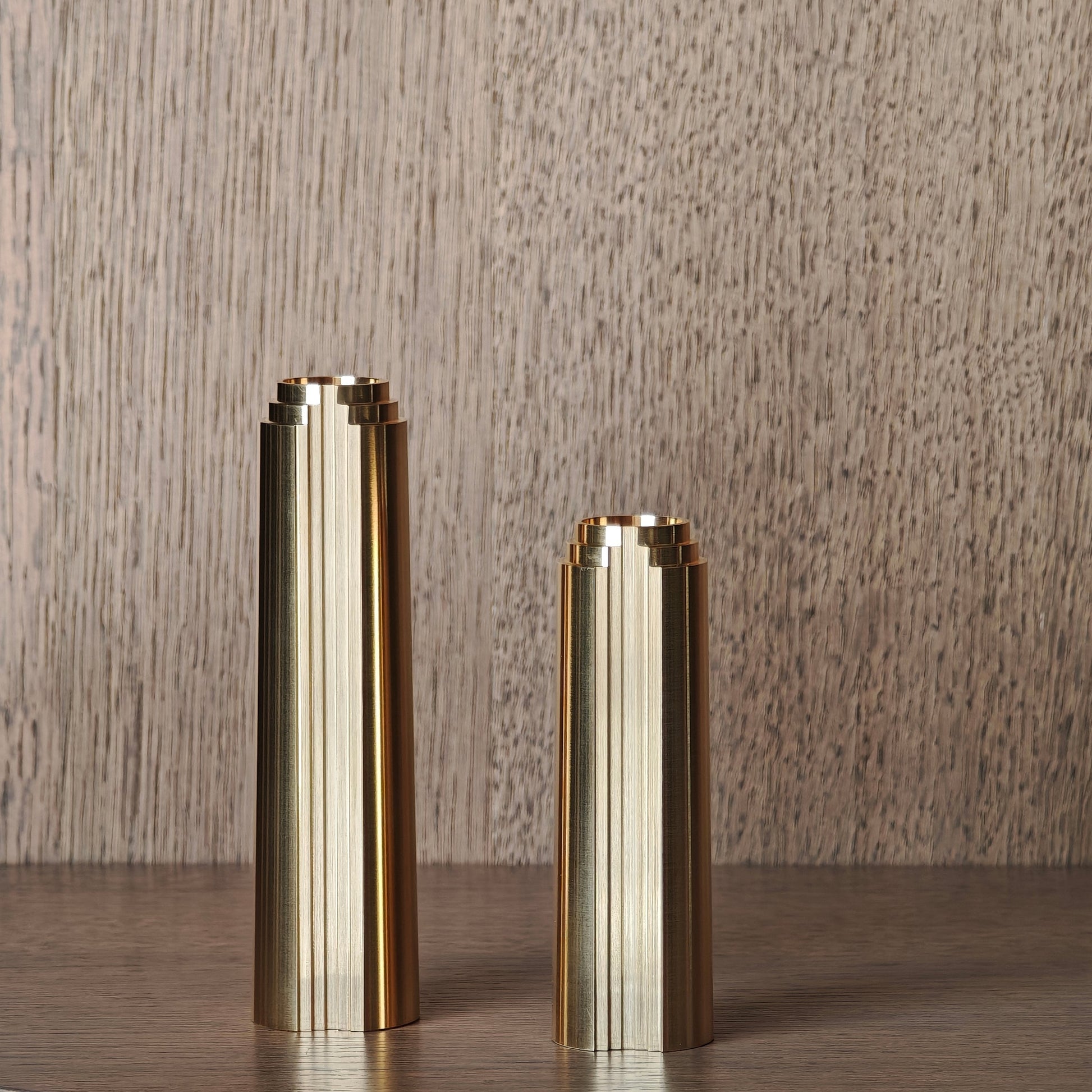 Two brass cylindrical candle holders on a wooden surface with a wooden background