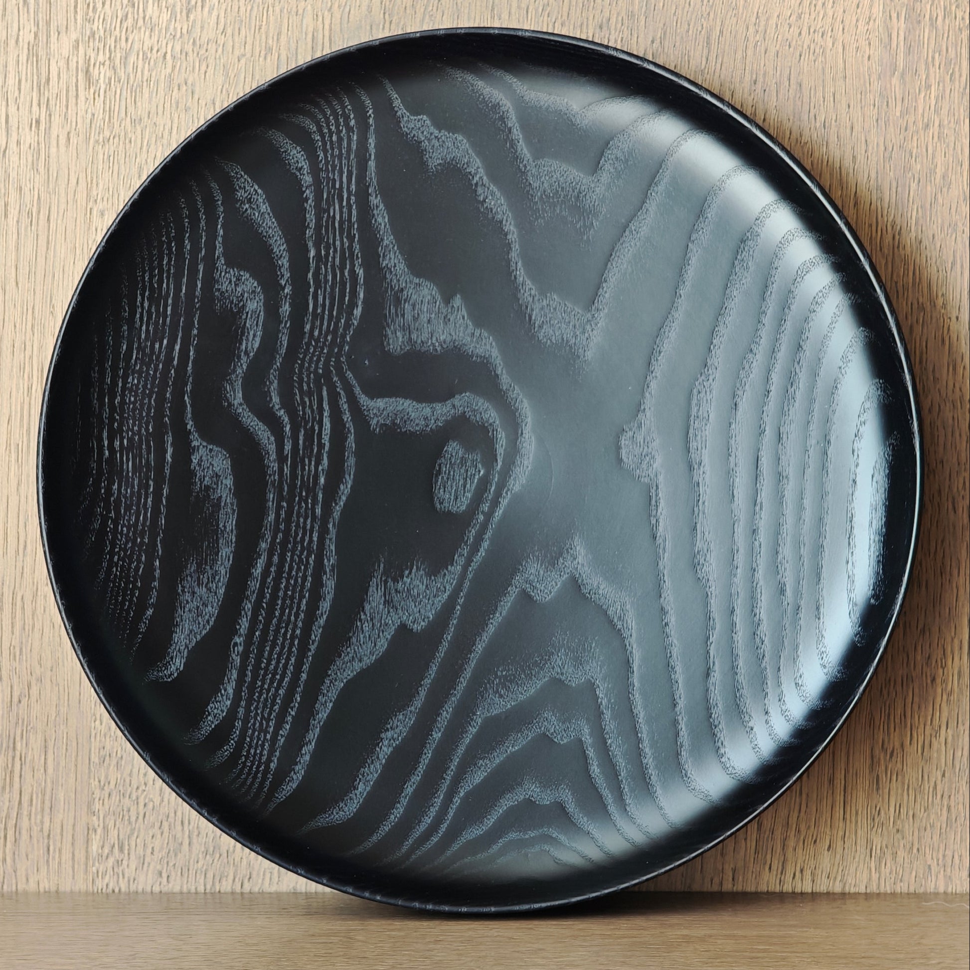 Black wooden plate with exposed pattern on a wooden surface