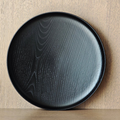 Black ash wood plate on a wooden surface