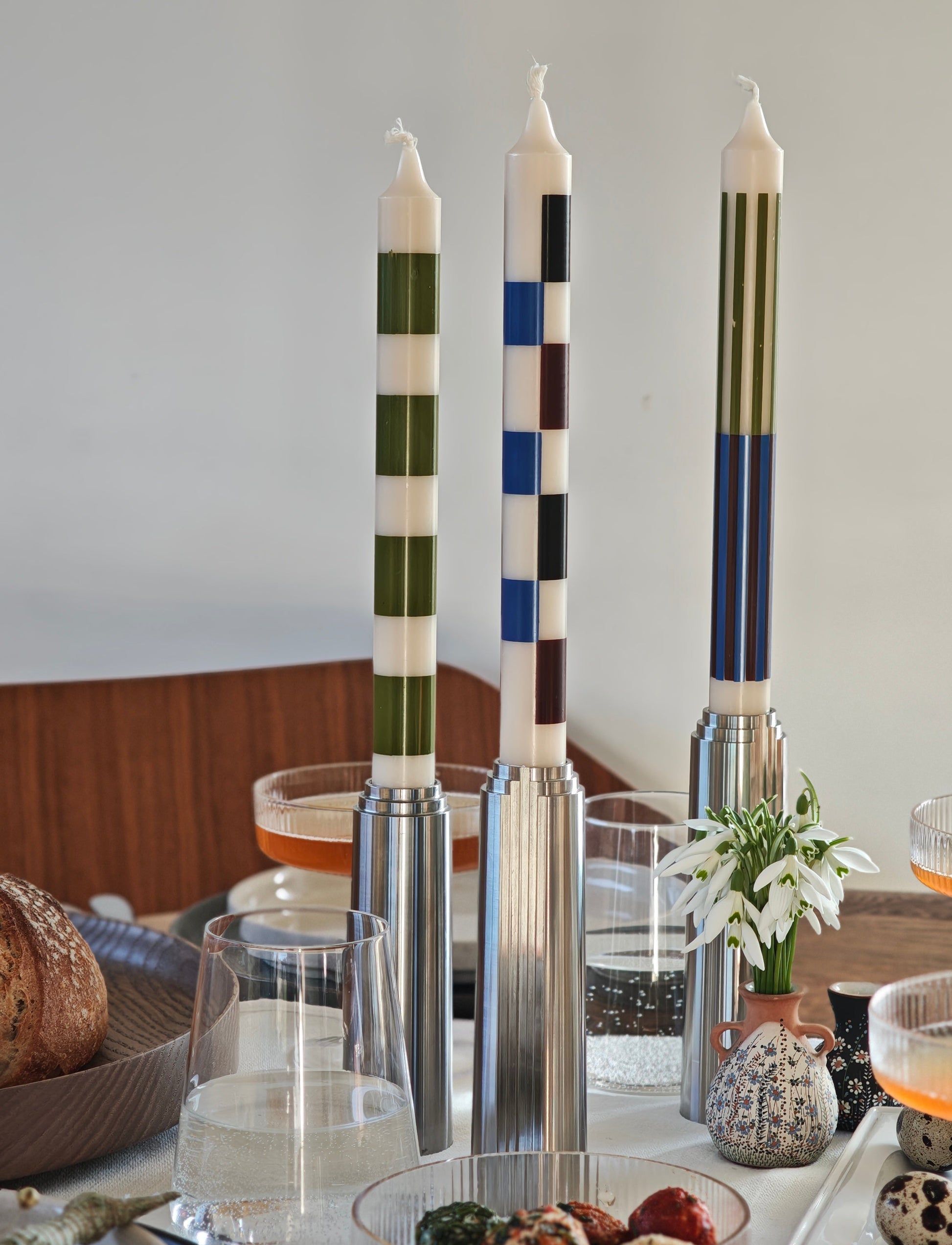 Stainless steel candlesticks with decorative check pattern candles on a table setting.